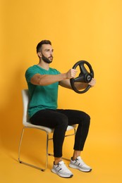 Photo of Serious man on chair with steering wheel against yellow background