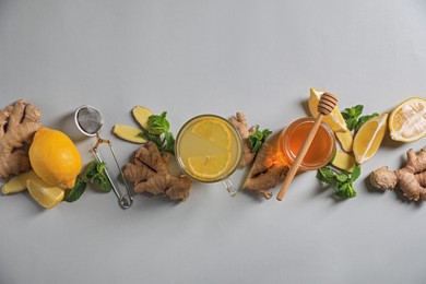 Glass of aromatic ginger tea and ingredients on light grey background, flat lay