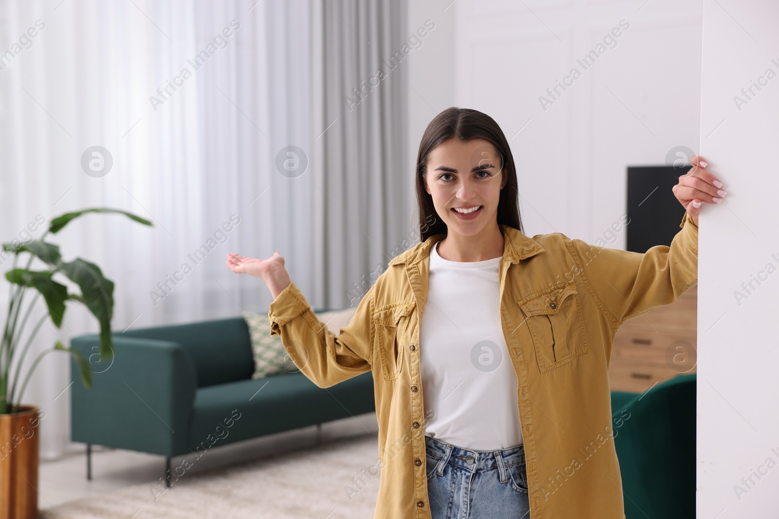 Photo of Happy woman welcoming near white wall at home, space for text. Invitation to come in room