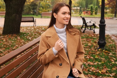 Beautiful young woman wearing stylish clothes on bench in autumn park