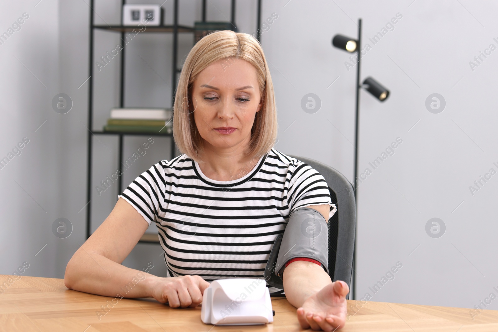 Photo of Woman measuring her blood pressure with tonometer at wooden table indoors