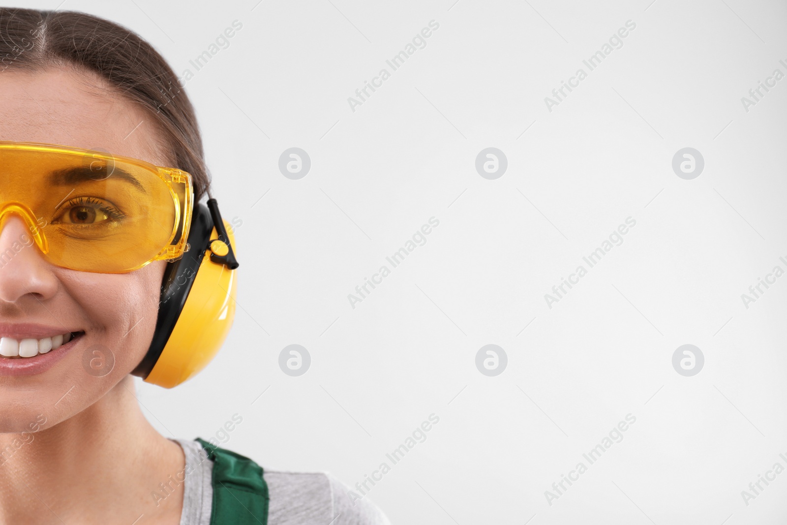 Photo of Female industrial worker in uniform on light background, space for text. Safety equipment