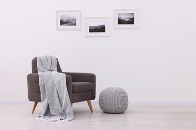 Photo of Comfortable armchair, blanket and pouf near white wall indoors. Space for text