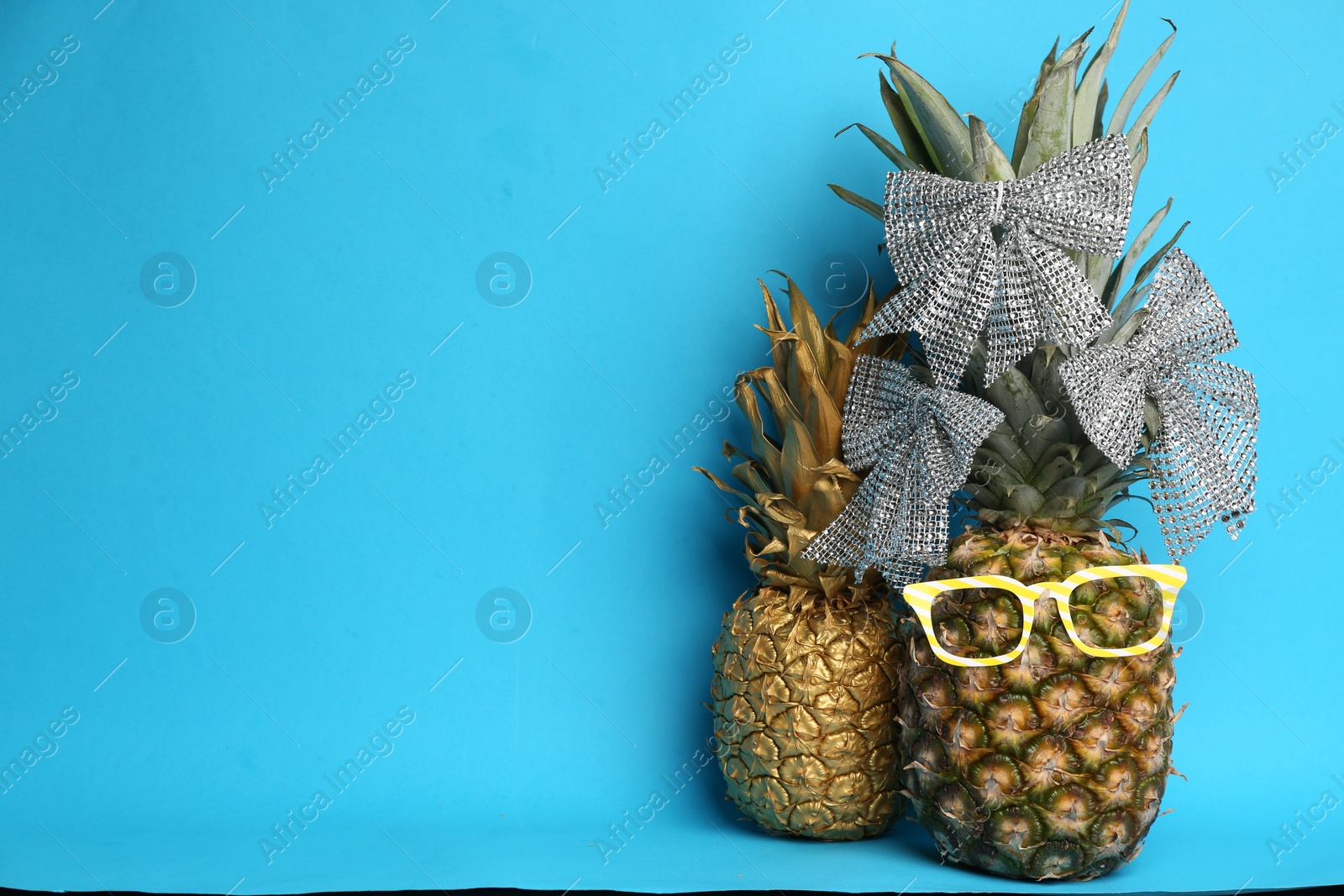 Photo of Decorated pineapples on light blue background, space for text. Creative concept