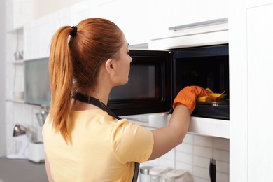 Woman cleaning microwave oven with rag in kitchen