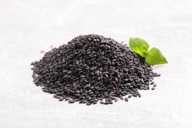 Photo of Pile of black sesame seeds and green leaf on light table, closeup