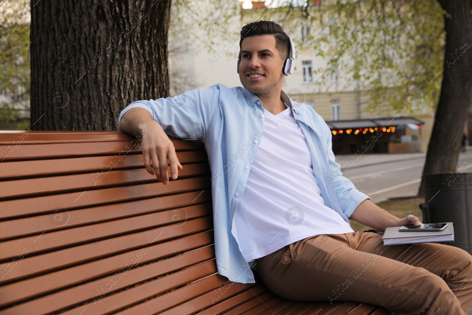 Photo of Happy man listening to audiobook on bench outdoors