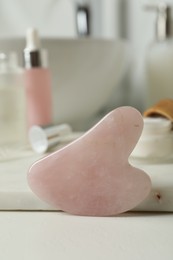 Rose quartz gua sha tool and toiletries on white countertop in bathroom, closeup