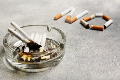 Ashtray with burnt butts and word No made of cigarettes on grey table, closeup. Stop smoking concept