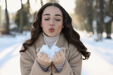 Photo of Portrait of beautiful woman blowing snow from hands in park