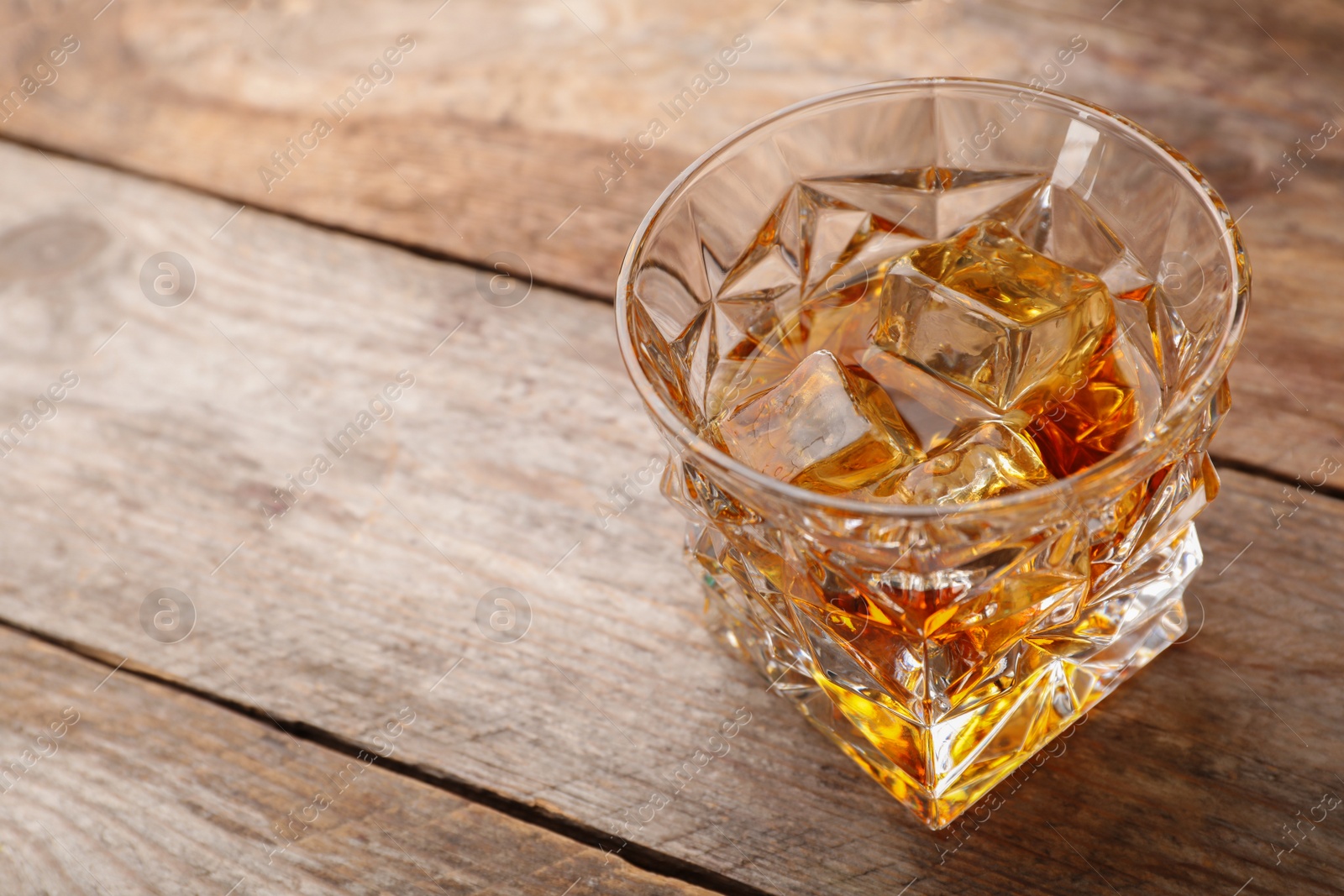 Photo of Golden whiskey in glass with ice cubes on table. Space for text