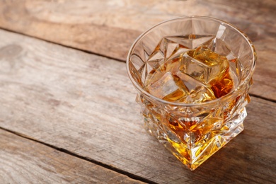 Photo of Golden whiskey in glass with ice cubes on table. Space for text