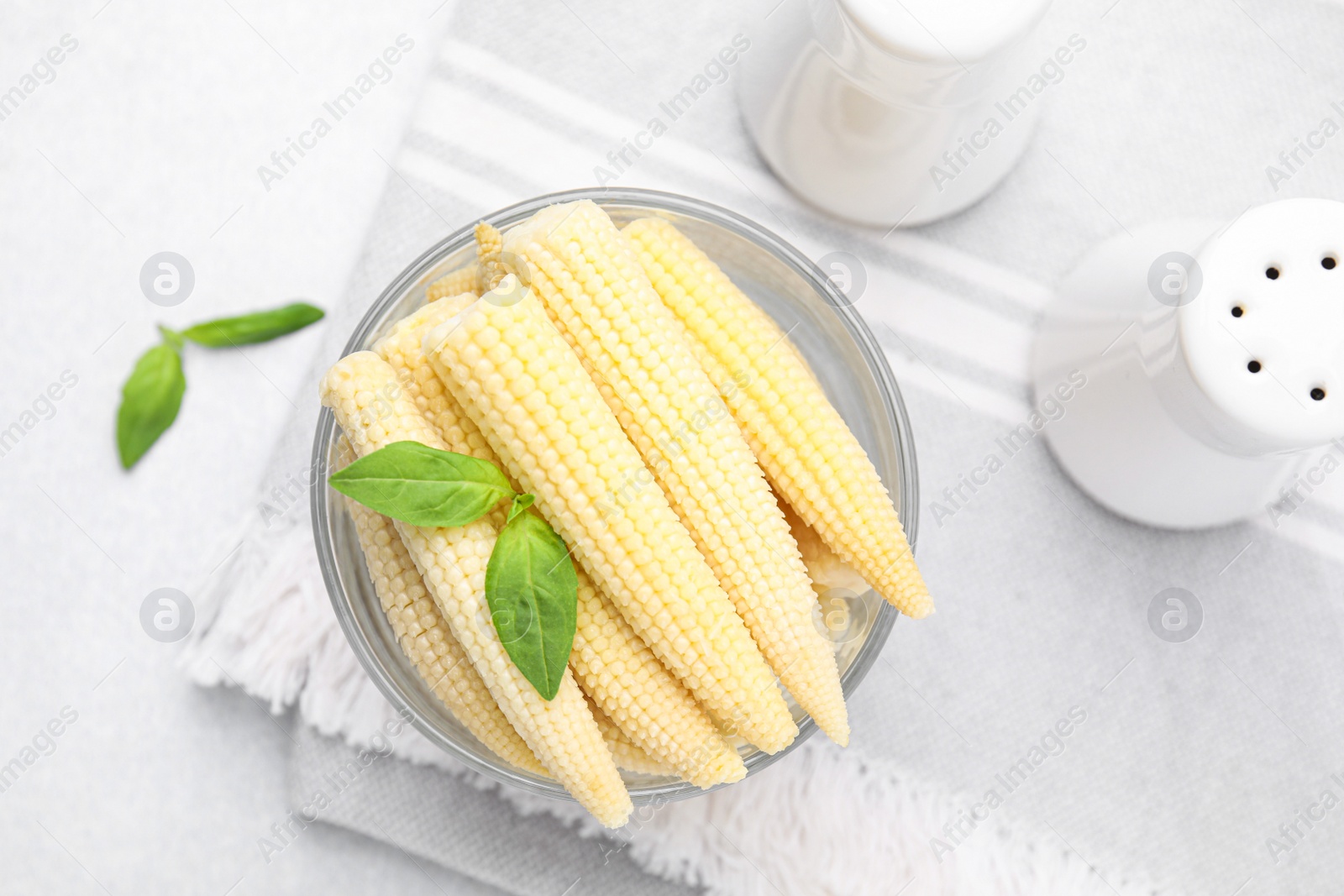 Photo of Canned baby corns with basil on light grey table, flat lay