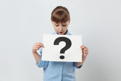 Photo of Emotional girl holding sheet of paper with question mark on white background