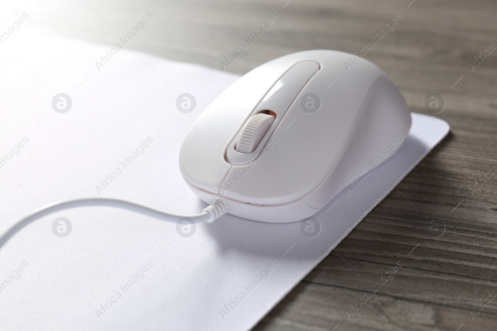 Photo of Wired mouse and mousepad on wooden table, closeup