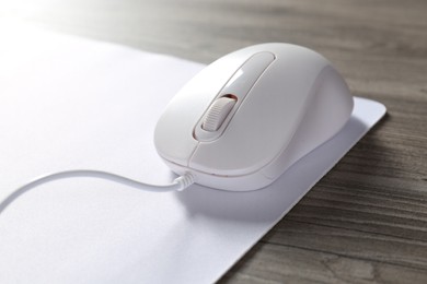 Photo of Wired mouse and mousepad on wooden table, closeup
