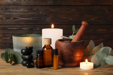 Aromatherapy. Scented candles, bottles, eucalyptus branches and mortar on wooden table