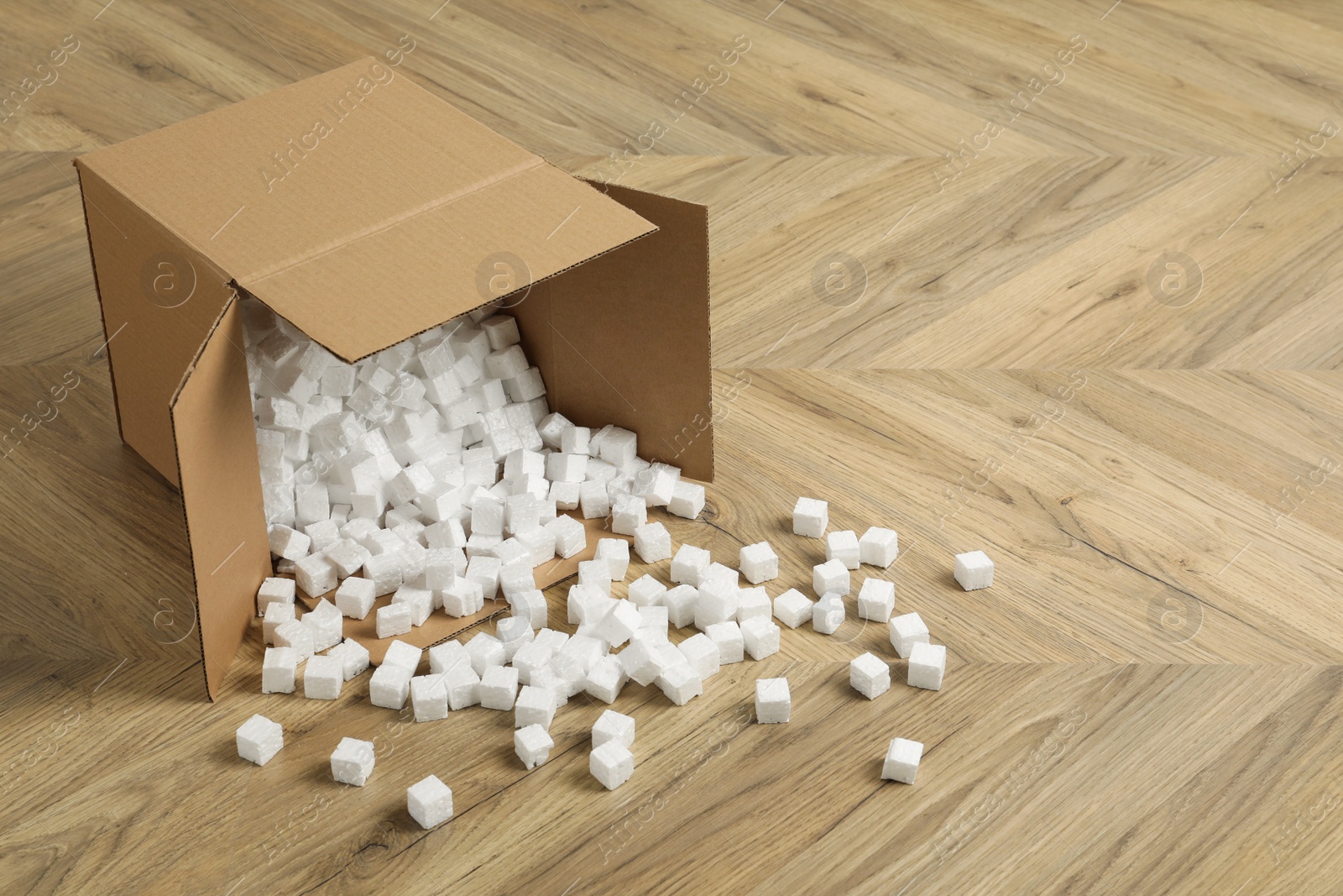 Photo of Overturned cardboard box with styrofoam cubes on wooden floor. Space for text