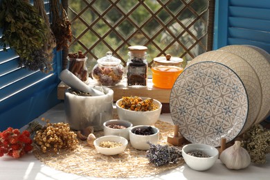 Many different dry herbs, flowers and plates on white wooden table near window