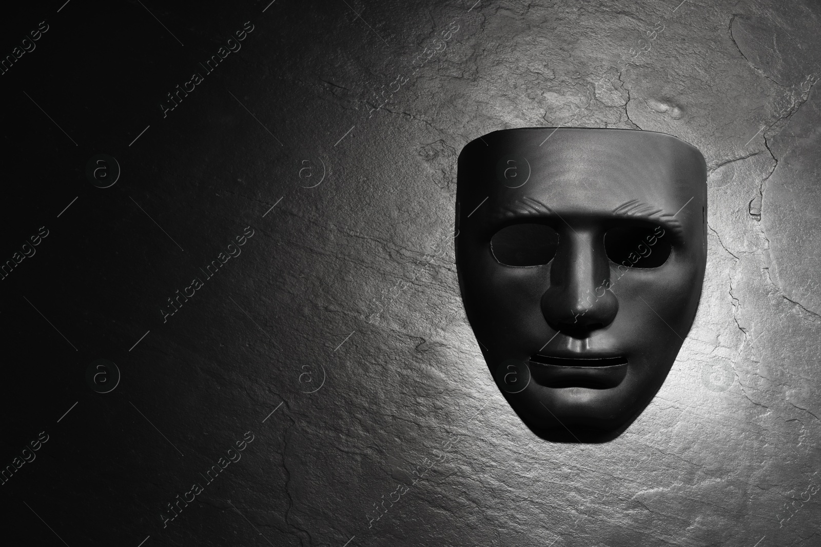 Photo of Plastic face mask on black slate surface, top view and space for text. Theatrical performance