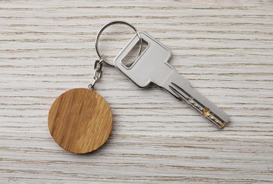 Photo of Key with keychain in shape of smiley face on light wooden background, top view