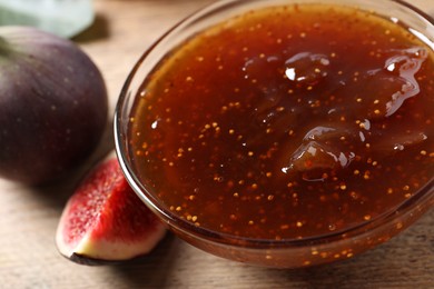 Bowl with tasty sweet jam and fresh figs on wooden table, closeup