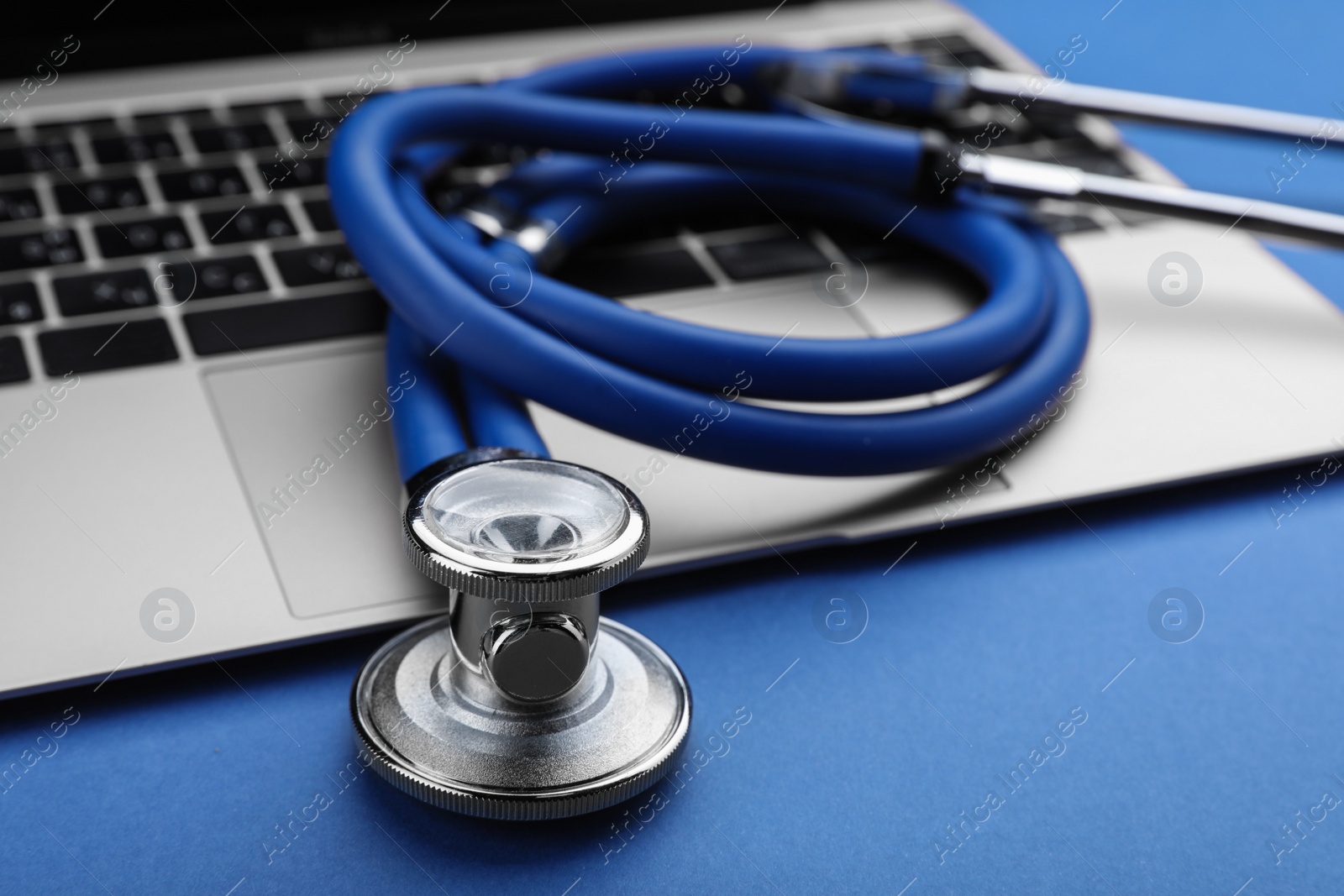 Photo of Laptop with stethoscope on blue background, closeup