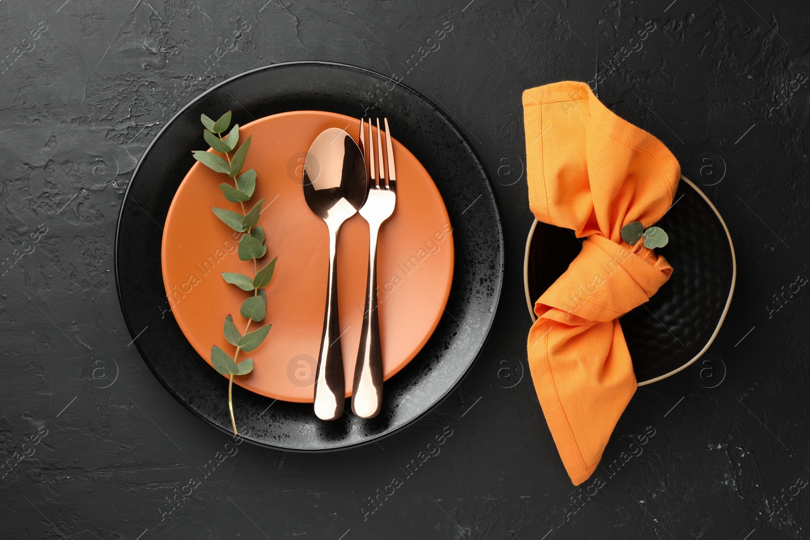 Photo of Stylish setting with cutlery, eucalyptus branch, napkin and plates on dark textured table, flat lay