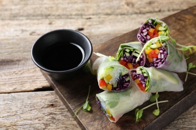 Photo of Delicious spring rolls and soy sauce on wooden table