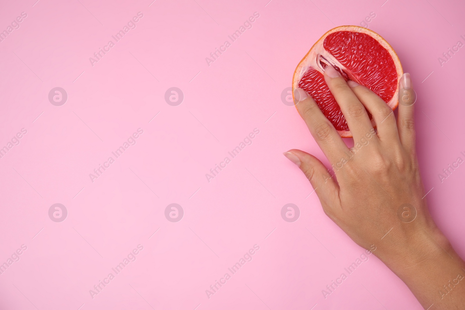Photo of Young woman touching half of grapefruit on pink background, top view with space for text. Sex concept
