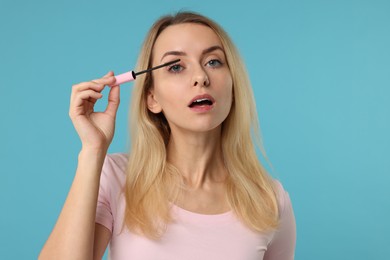 Photo of Beautiful woman applying mascara on light blue background