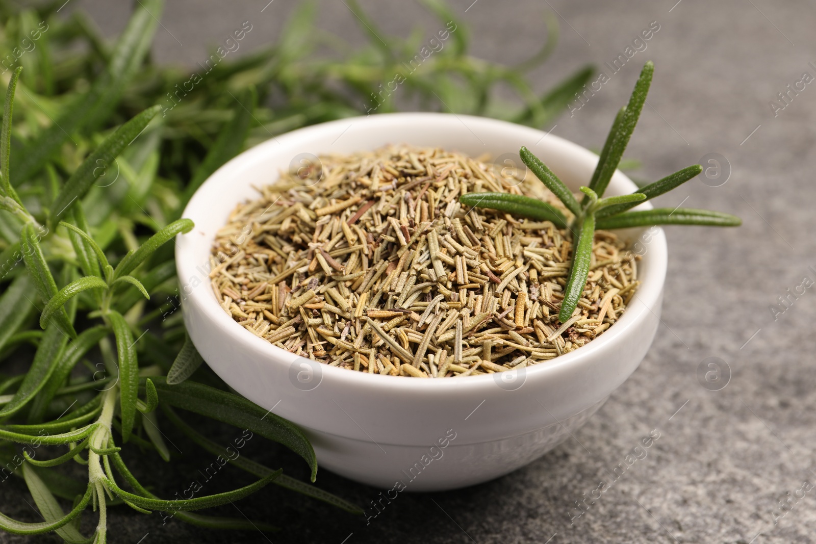 Photo of Dry and fresh rosemary in bowl on gray table, closeup