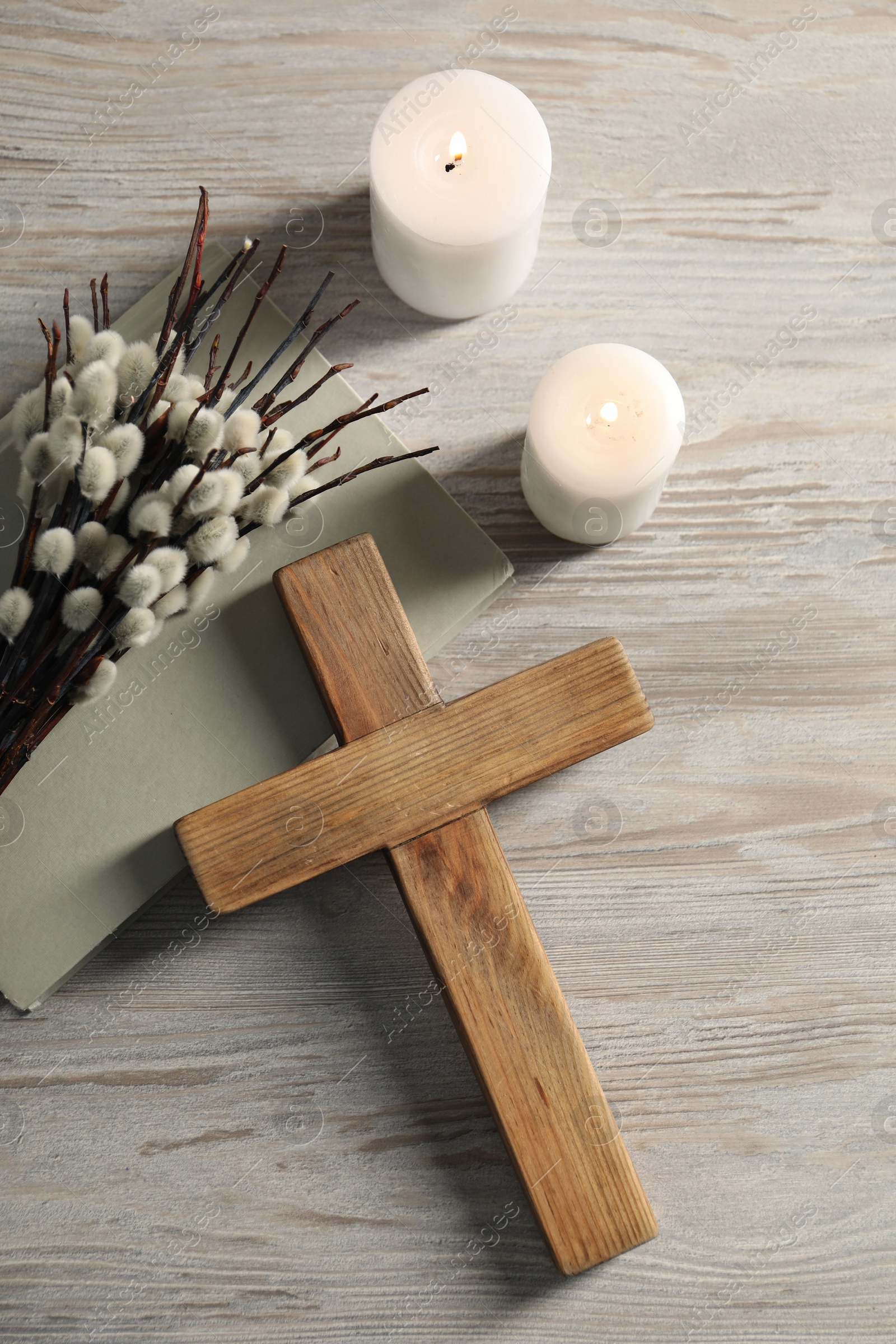 Photo of Burning candles, cross, book and willow branches on wooden table, flat lay