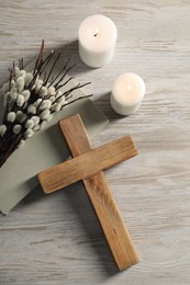 Photo of Burning candles, cross, book and willow branches on wooden table, flat lay