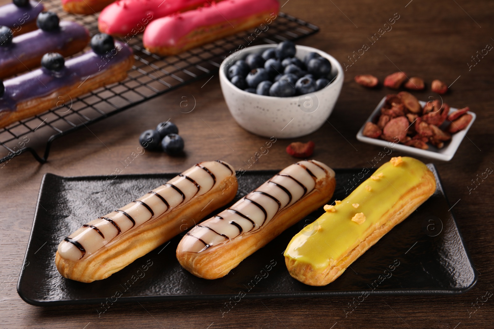 Photo of Different tasty glazed eclairs on wooden table, closeup