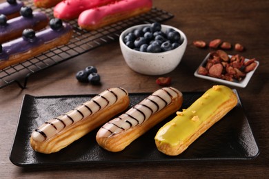 Photo of Different tasty glazed eclairs on wooden table, closeup