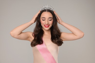 Photo of Beautiful young woman with tiara and ribbon in dress on grey background. Beauty contest