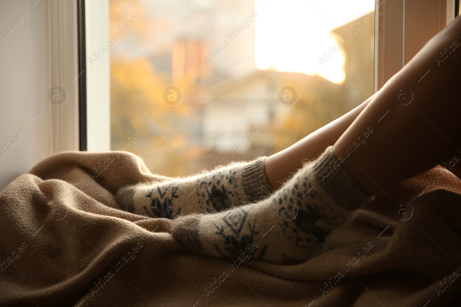 Photo of Woman in knitted socks relaxing on plaid near window at home, closeup