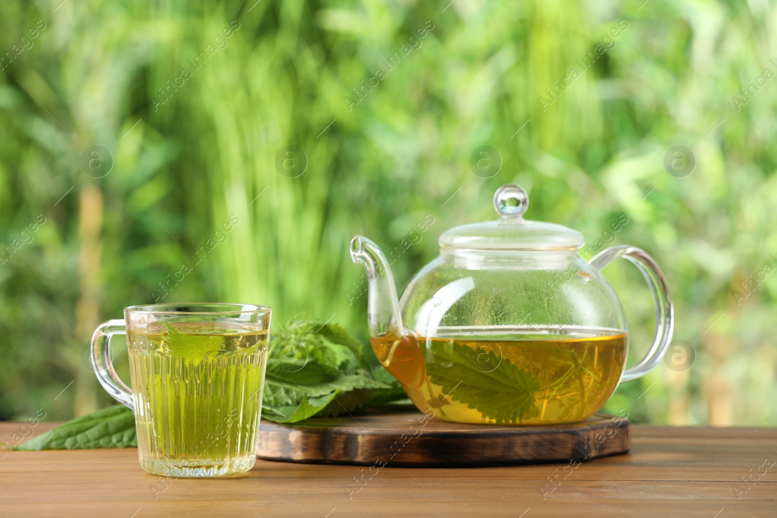 Photo of Aromatic nettle tea and green leaves on wooden table outdoors