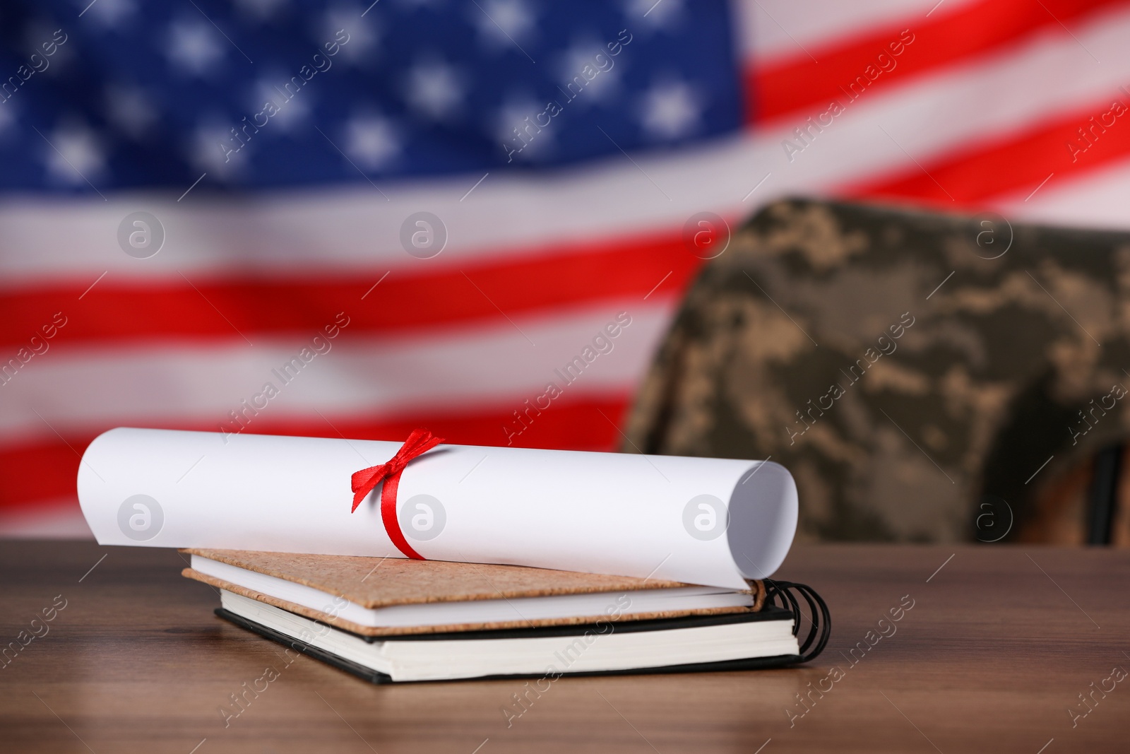 Photo of Diploma and notebooks on wooden table against flag of USA. Military education