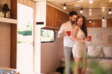 Happy young couple with cups in trailer. Camping vacation