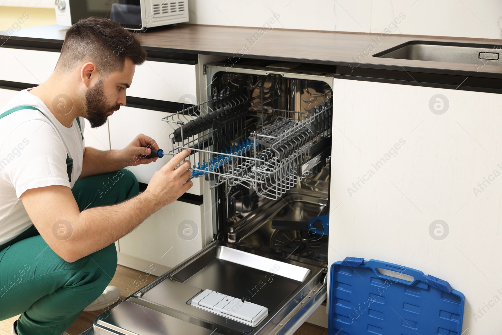 Photo of Serviceman repairing dishwasher with screwdriver in kitchen