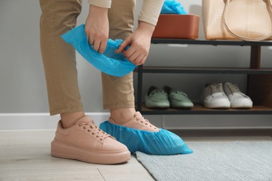 Photo of Woman wearing blue shoe covers onto her sneakers indoors, closeup