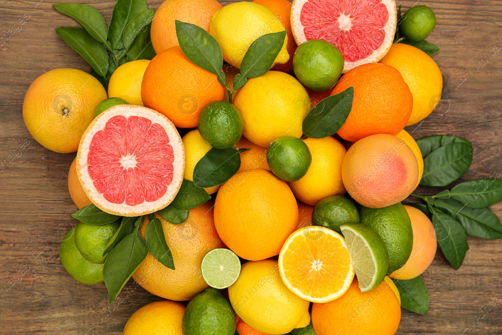 Photo of Different citrus fruits with green leaves on wooden table, flat lay