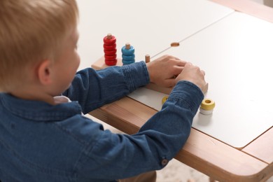 Photo of Little boy playing with stacking and counting game at table indoors, selective focus. Child's toy