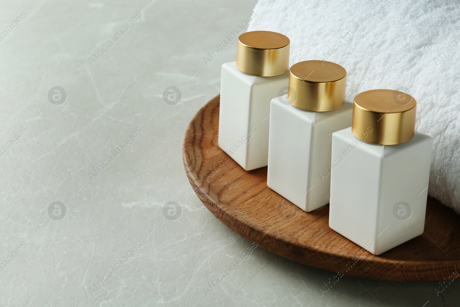 Photo of Wooden tray with cosmetic bottles and towel on light grey marble table, space for text. Spa treatment