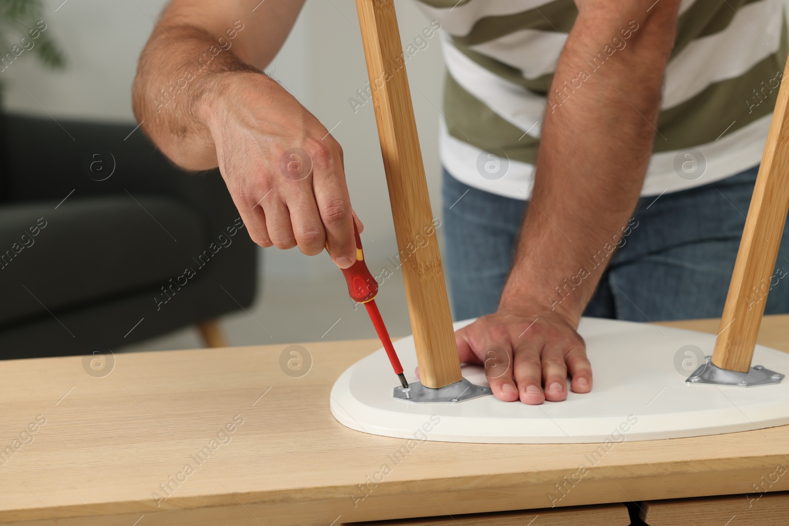 Photo of Man with screwdriver assembling stool at table indoors, closeup