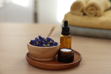 Photo of Bottle of essential oil, dry flowers and jar with cream on light wooden table. Spa therapy