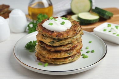 Photo of Delicious zucchini pancakes with sour cream served on white wooden table