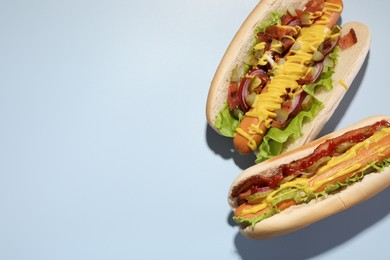 Photo of Delicious hot dogs with bacon, lettuce, onion and pickle on light blue background, flat lay. Space for text